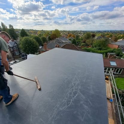 Roofer applying EPDM with roller on flat roof