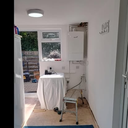 Utility room with boiler on wall and bare floor