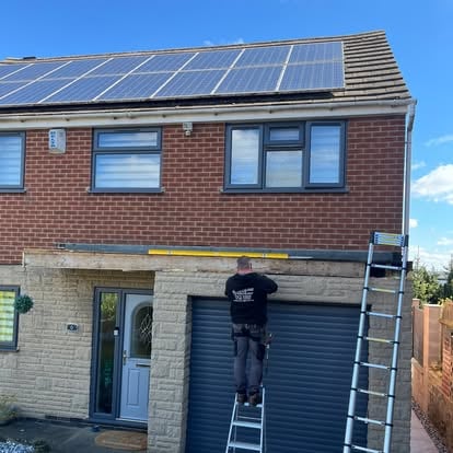 Worker on ladder fitting fascia at solar panel house garage