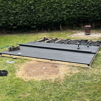 Grey composite deck being installed in hedge garden