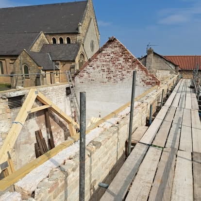 Stone building and scaffolding with church behind