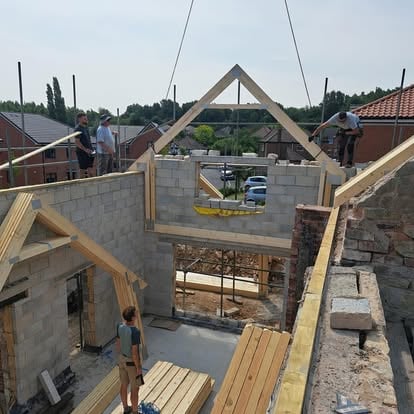 Workers positioning roof trusses on blockwork extension