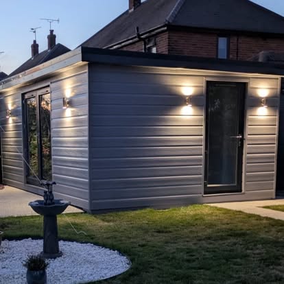 Grey cladding garden room at dusk with wall lights